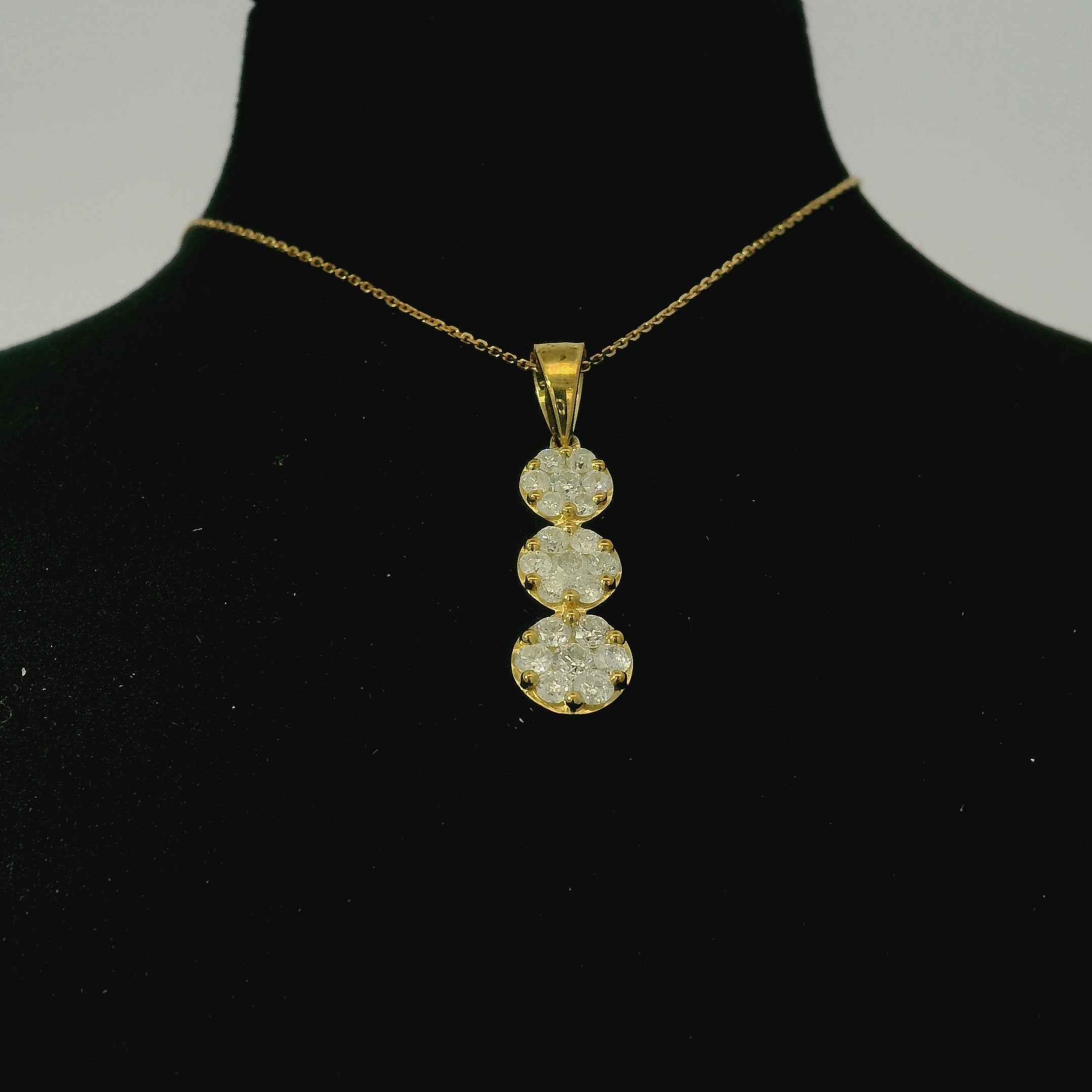 Gold necklace with a three-stone diamond pendant on a black mannequin.