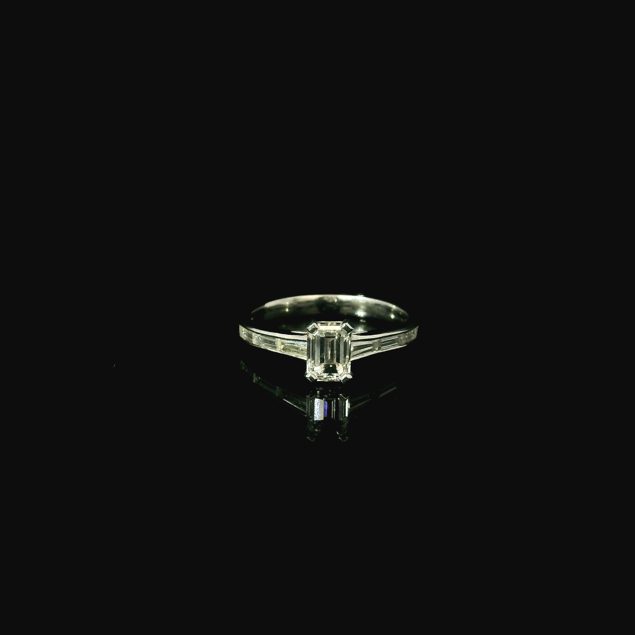 Diamond ring with emerald-cut gemstone on a black background